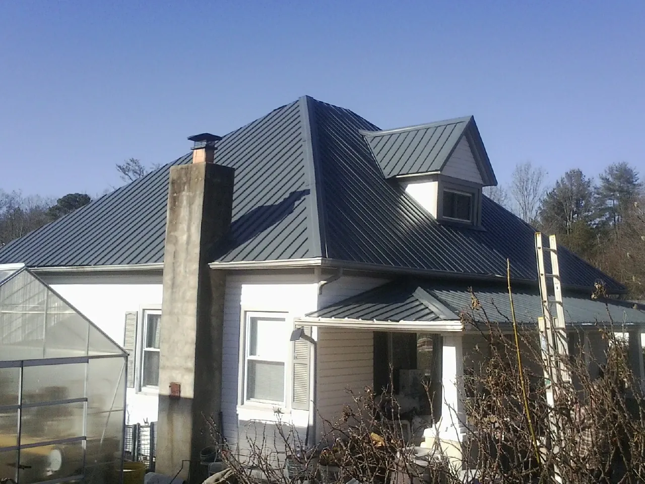 Dark blue standing seam metal roof on a white farmhouse with dormer — Slate & Tile Roof Repair by Roofing Brothers in Hornbeak