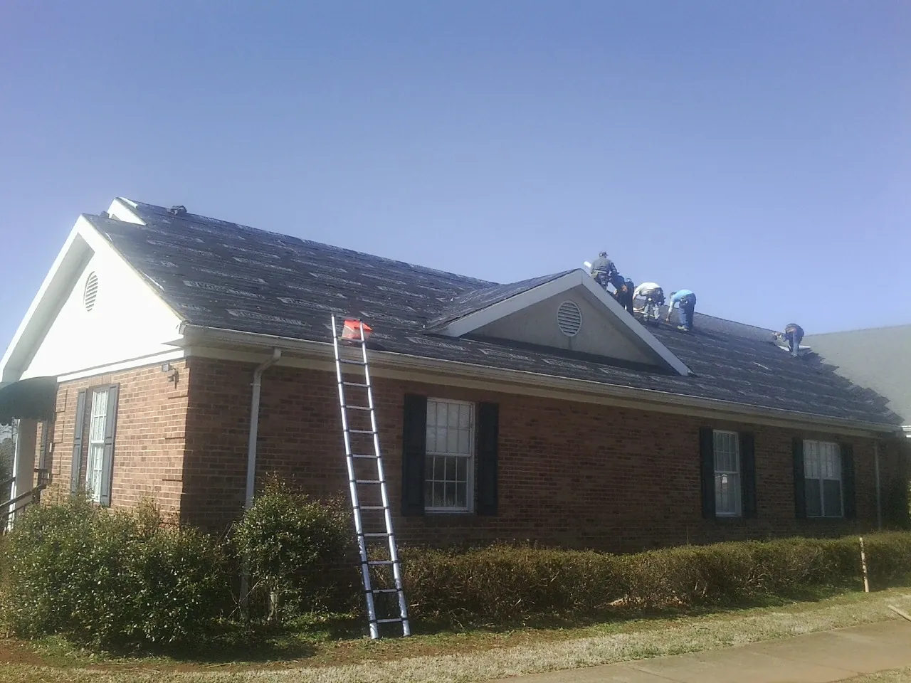 Crew tearing shingles off a brick ranch roof with a ladder set — Emergency Roof Repair work by our crew in Hornbeak