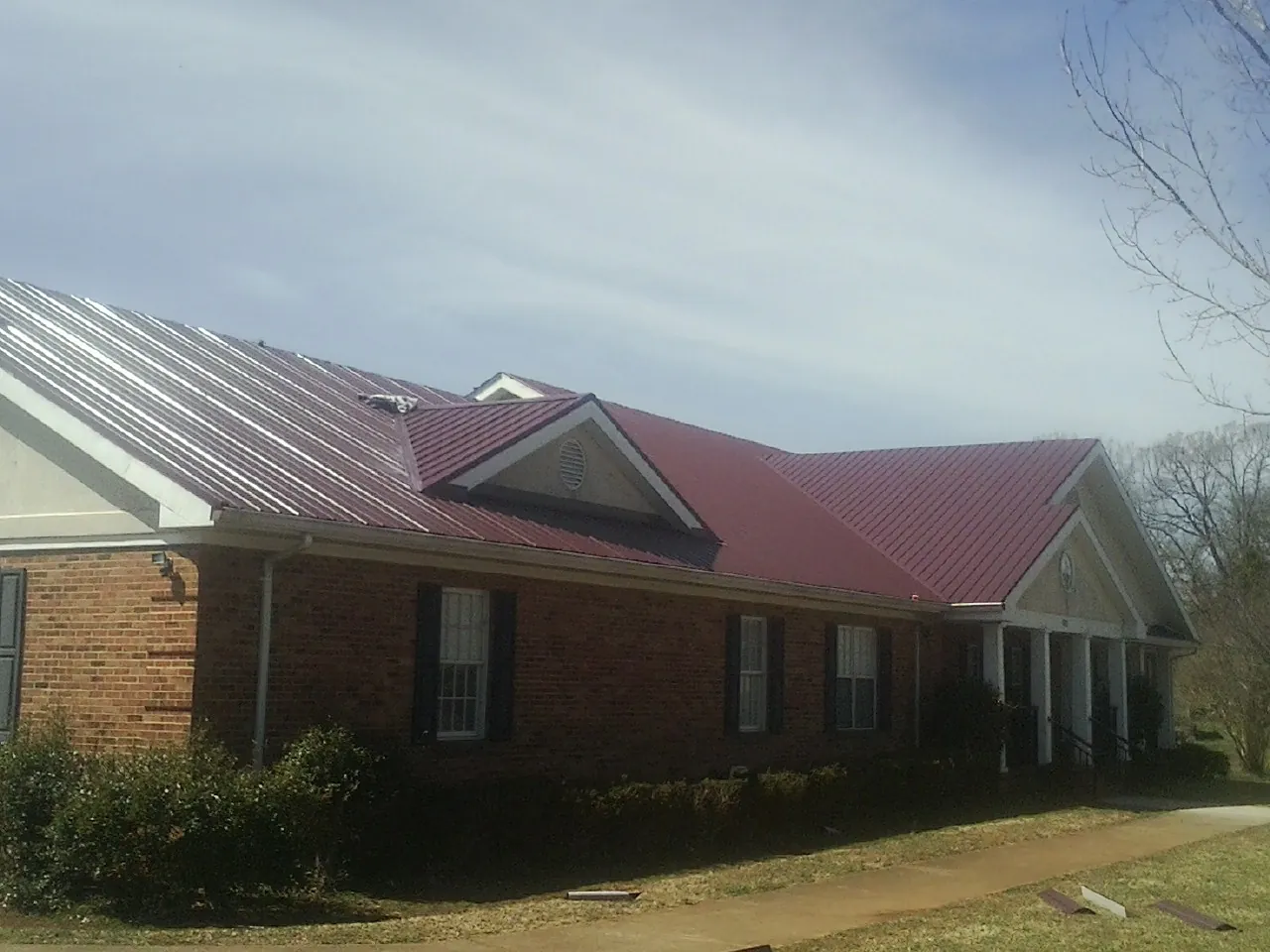 Red metal roof with gabled entries on a long brick building, from a Hail Damage Roof Repair job in Hornbeak