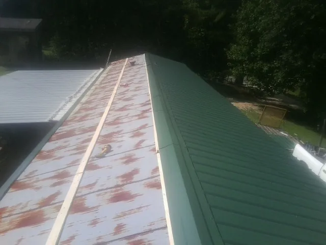 Old rusted panels beside newly installed green metal roofing — Wind Damage Roof Repair by Roofing Brothers in Hornbeak