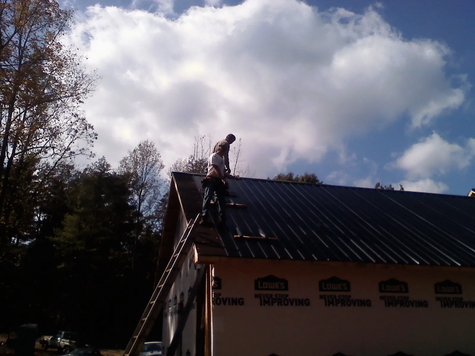 Roofer fastening dark metal panels high against a cloudy sky, from a Roof Inspection job in Hornbeak