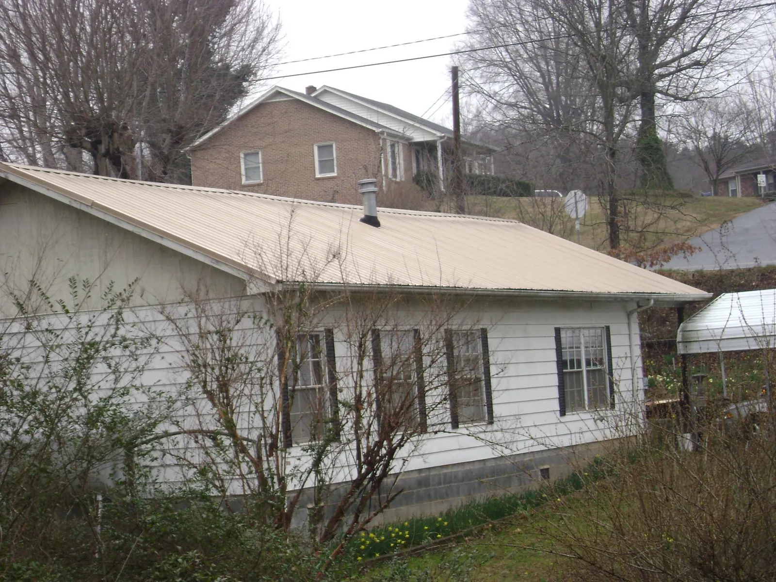 Tan metal roof on a white sided house set into a hillside — Commercial Roofing by Roofing Brothers in Hornbeak