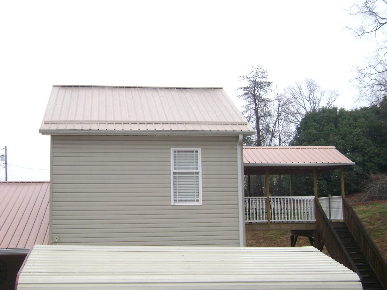 Tan metal roofs on a two story addition and attached porch, from a Roof Replacement job in Hornbeak